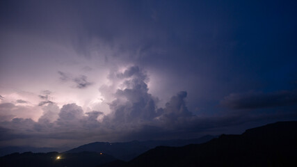 Evening thunderstorm with lightning in the mountains. Dramatic clouds during a thunderstorm pierce the light of lightning in a mountainous area. - obrazy, fototapety, plakaty