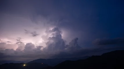 Foto op Plexiglas Evening thunderstorm with lightning in the mountains. Dramatic clouds during a thunderstorm pierce the light of lightning in a mountainous area. © Niko_Dali