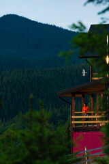 a girl in an orange jacket stands on the terrace of a wooden house against the background of...