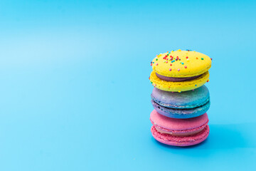 Brightly colored stacked macarons on blue background. Tasty colorful macaroon assorted. French...