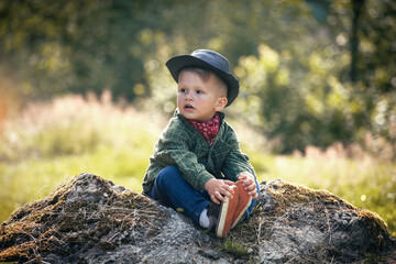 Cute Little Boy with Hat and Checkered Shirt Sitting in Summer Forest - 741386768