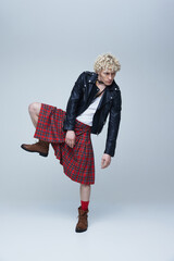 Fusion of cultures. Full length portrait of man in Scottish kilt and punk leather jacket posing...