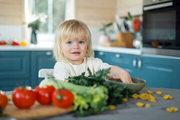 Adorable toddler girl playing with vegetables in a bright kitchen.