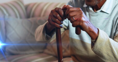 Image of light moving over senior asian man at home on couch using walking stick