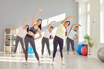 Group of happy smiling young beautiful women doing stretching exercises at a fitness workout at a modern gym. Sport, working out, wellness, healthy lifestyle concept