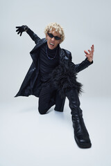 Young man in total-black, leather-heavy outfit rocking out with annoying expression against grey...