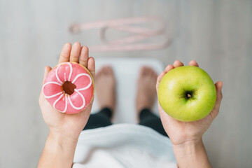 woman on weight scale and hand hold green Apple and donut, choose between fruit is Healthy and...