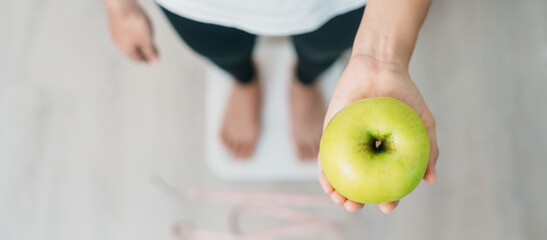 woman on weight scale and hand hold green Apple, choose fruit is Healthy food. Dieting control,...
