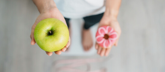woman on weight scale and hand hold green Apple and donut, choose between fruit is Healthy and sweet is Unhealthy junk food. Dieting control, Weight loss, Obesity, eating lifestyle and nutrition - obrazy, fototapety, plakaty
