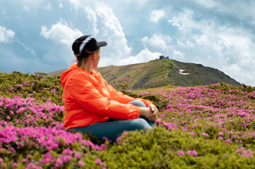 The girl is sitting on the meadow of the Carpathians with rhododendrons.