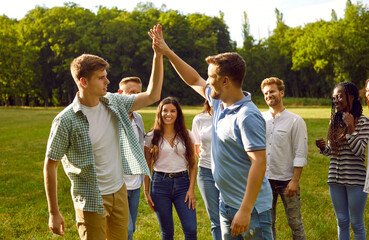 Group of a happy young people walking in the summer park giving high five greeting each other...