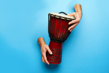 Male hands sticking out blue background and playing djembe. World music festival poster featuring...