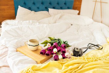 Fototapeta na wymiar Coffee cup and bouquet of tulips on the bed