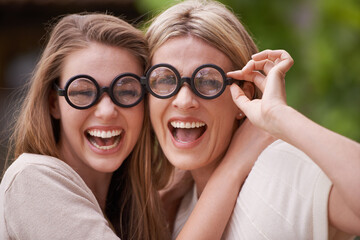 Women, mother and daughter with funny glasses in garden for comic joke, laughing and hug in...