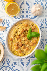 A bowl of hummus with chickpeas and basil on a table