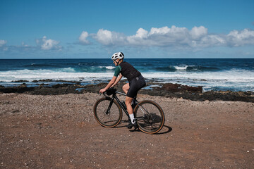 Woman cyclist riding a gravel bicycle a gravel road with beautiful view on Atlantic ocean on Tenerife, Canary Islands, Spain. Sport motivation. Cycling training outdoors in Spain. Cycling adventure.