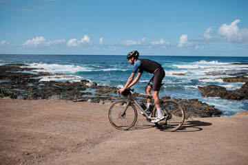 Fototapeta premium Male cyclist, dressed in a black cycling kit and helmet, is training on a gravel bike in the mountains,enjoying an amazing view. Man cyclist is riding downhill on the Transalpina road.Parâng Mountains