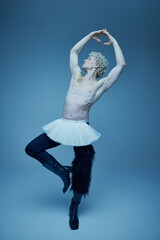 Shirtless man in tutu and boots posing in ballet pose against grey studio background, embodying...