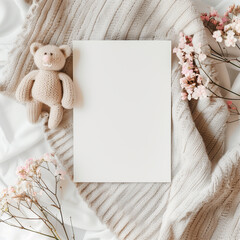 Top view of teddy bear beside blank paper with pink blossoms, ideal for invitations.