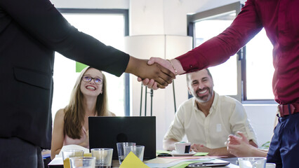 A group of individuals seating around a table engaging in handshakes as a form of greeting or...