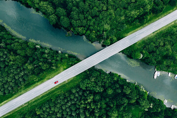 Aerial view of bridge road with car over blue river and green woods in Finland