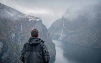 Traveler with his back turned, enjoying a mountain landscape in the Norwegian fjords of Geiranger,...