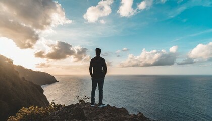 A man stands on a mountain. He can be seen as a silhouette. In the background is the sea