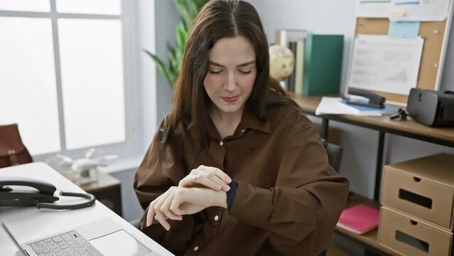 A young woman sits in an office, smiling while checking her smartwatch, embodying a blend of professionalism and modernity.