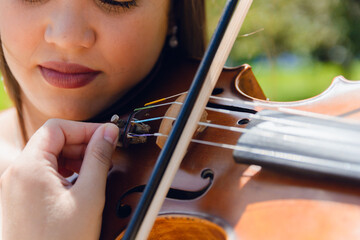 closeup of young busker woman tuning violin outdoors