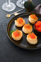 Salmon red caviar toast. Christmas canape or toast with red caviar on black plate on dark background. Idea to xmas snack. Gourmet food. Texture of caviar. Seafood.