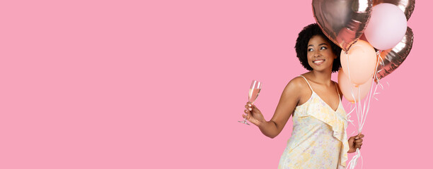 Cheerful African American woman with curly hair, holding balloons and a glass of sparkling wine - obrazy, fototapety, plakaty