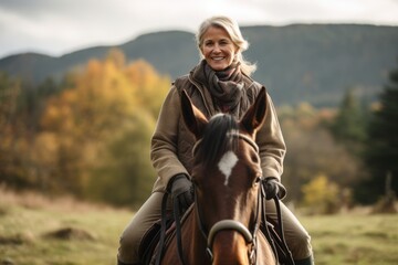 Senior woman riding a horse in the autumn forest. Outdoor portrait. - obrazy, fototapety, plakaty