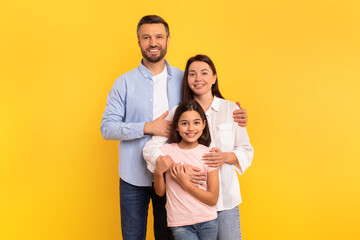 Fototapeta premium Millennial parents and their daughter posing in tender hug, studio