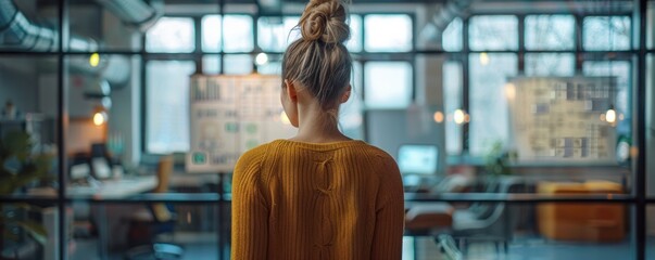 A young professional stands in contemplation in a modern workspace, surrounded by glass walls and a creative, organized atmosphere.