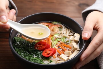 Woman eating delicious ramen with spoon at table, closeup. Noodle soup