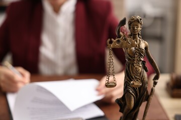 Notary signing document at table in office, focus on statue of Lady Justice