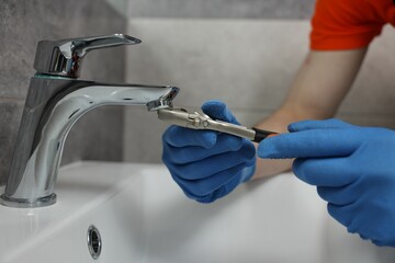 Plumber repairing faucet with spanner in bathroom, closeup
