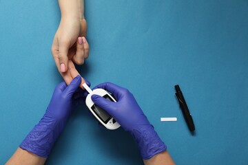 Diabetes. Doctor checking patient's blood sugar level with glucometer on blue background, top view