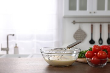Whisk, bowl, beaten eggs and other ingredients on wooden table indoors, space for text