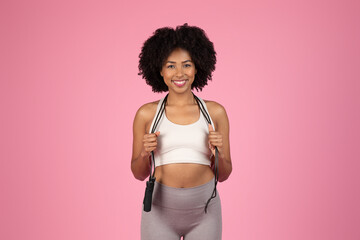Happy black fitness woman with jump rope on pink backdrop