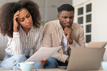 Frowning African American married couple using laptop doing paperwork indoor