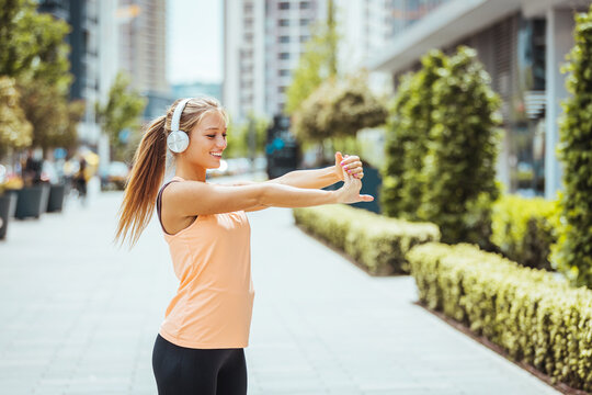 Woman stretching at park while listening to music. Young woman working out at sunset. Healthy sport girl doing stretching exercise early in the morning at park.