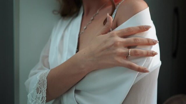 a beautiful young bride in a white dress with an open neckline hangs pearl jewelry on her neck and strokes her body, morning preparations before the wedding ceremony