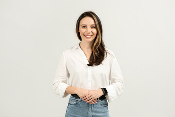 A confident young woman with long brown hair wearing a casual white blouse and blue jeans