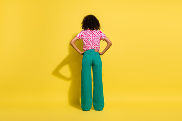 Full length rear behind portrait of young person put hands waist posing isolated on yellow color background