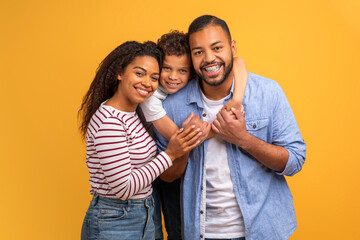 Positive black family with preteen son hugging and smiling at camera