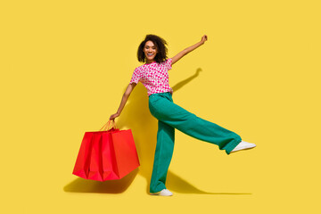 Full body portrait of cheerful overjoyed nice lady hold shop bags dance isolated on yellow color...