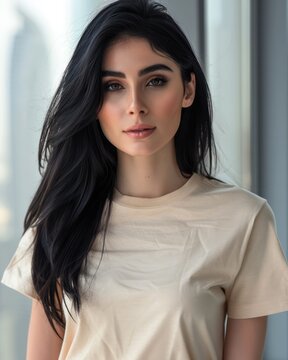A young Arabic woman with black hair wearing a beige shirt poses, facing the camera