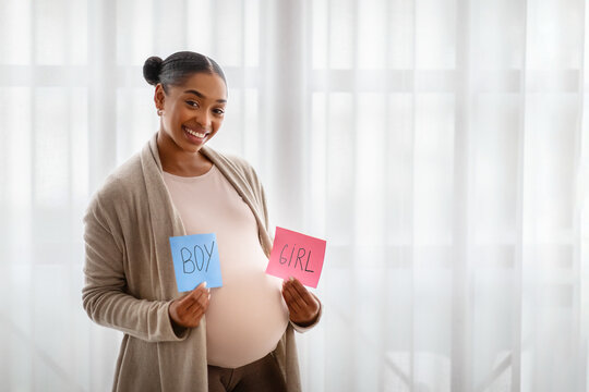 Positive african american pregnant woman showing boy and girl cards