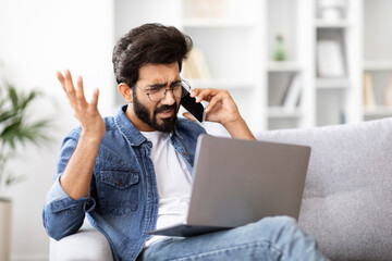 Annoyed indian man making confused gesture during stressful phone call at home
